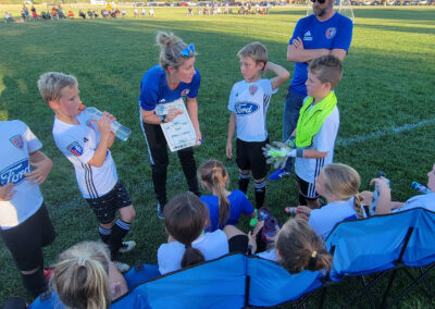 Hamilton North Futbol Club players attentively listening to their coach's guidance on the field.