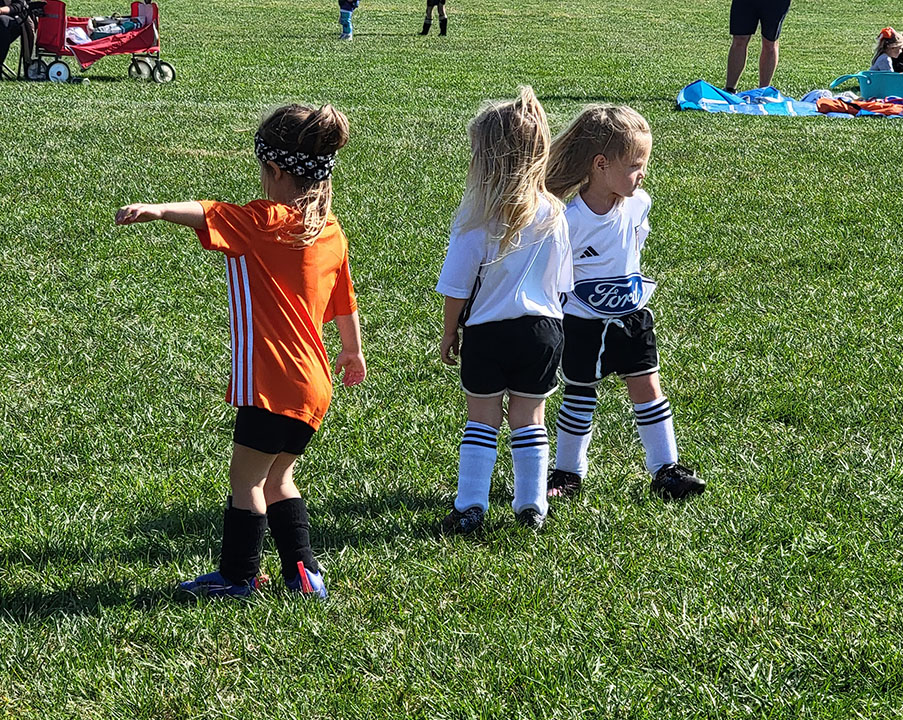 Hamilton North Futbol Club U6 players in orange and white jerseys playing on the field.